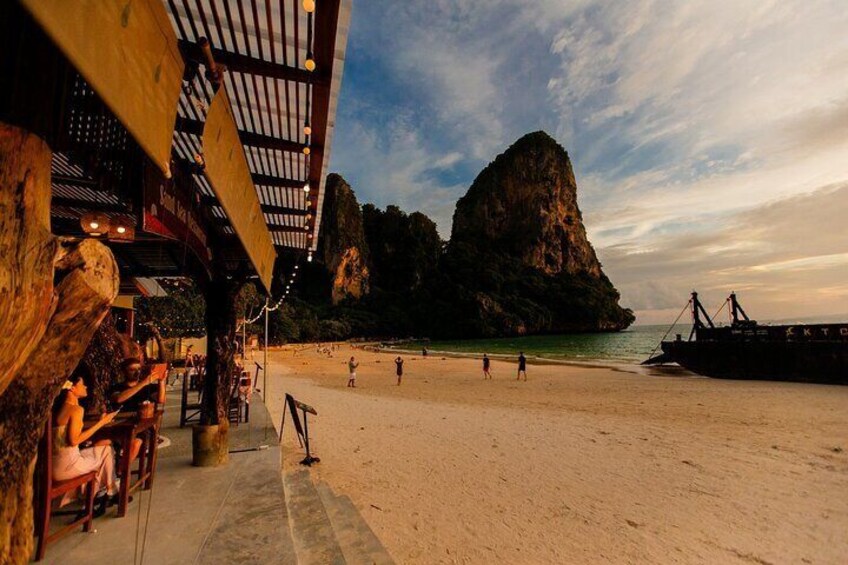 A beach with a wooden structure, a large rock formation, and a ship in the background. 3
