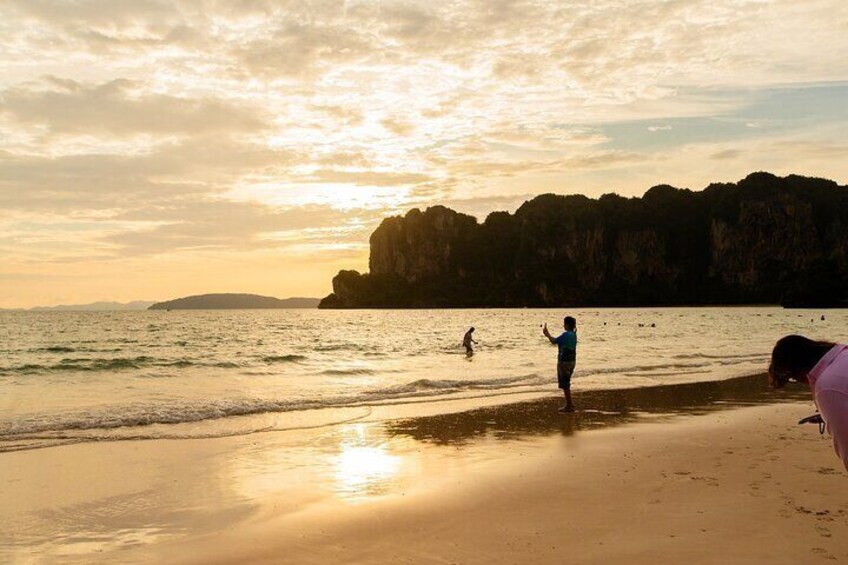 A beach at sunset with people near the water and cliffs in the background. 5
