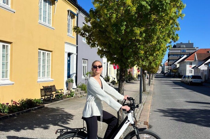 A person riding a bicycle on a street with buildings and a tree. 5
