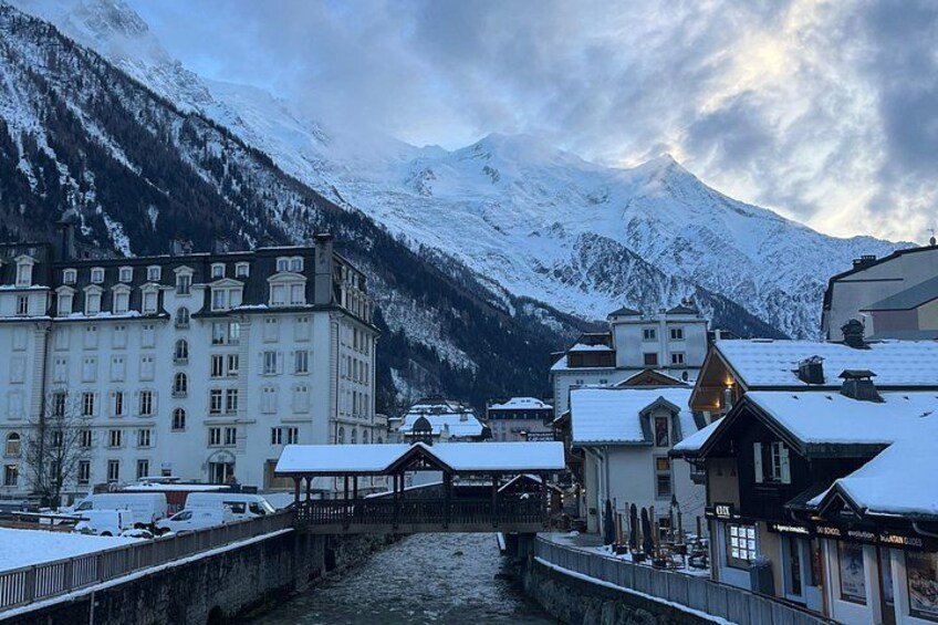 A snow-covered town with a river, buildings, and mountains in the background. 2