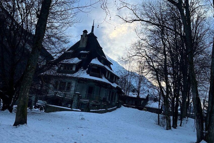 A snow-covered house with a steep roof, surrounded by bare trees and a snowy landscape. 3