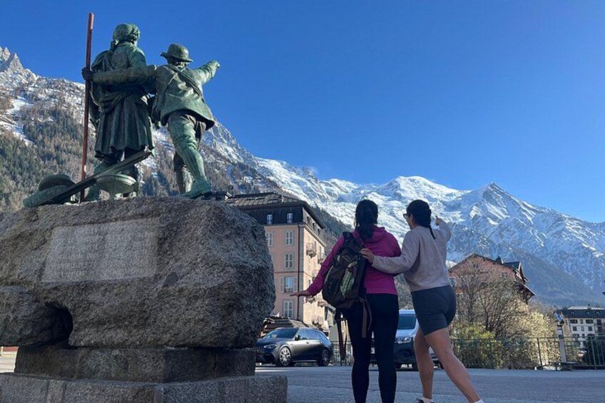 A statue of two figures on a rock, a snowy mountain in the background, and a building with a red roof. 5