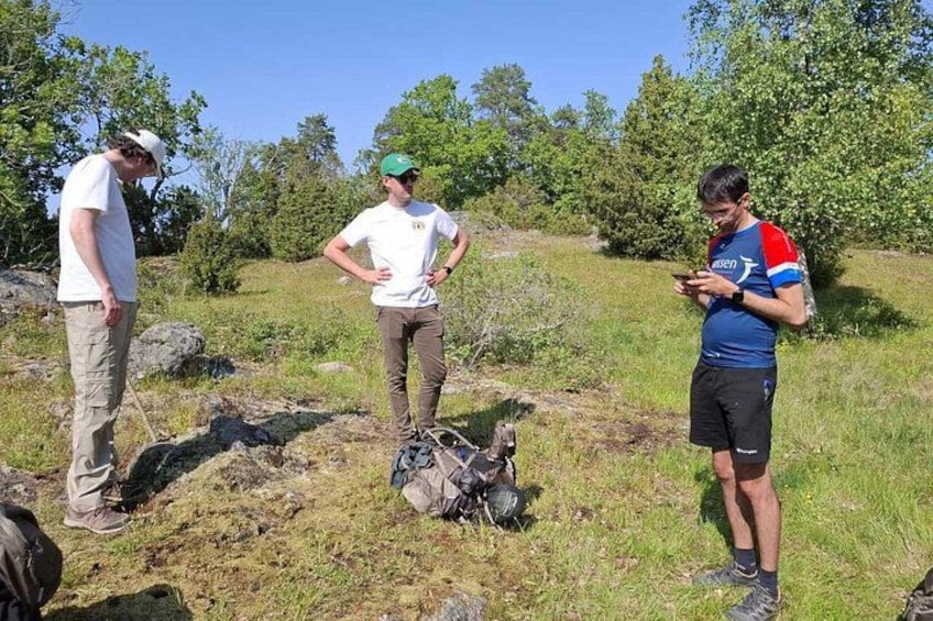 Tre persone all'aperto, una tiene in mano un dispositivo, con uno zaino e una borsa a terra. 2
