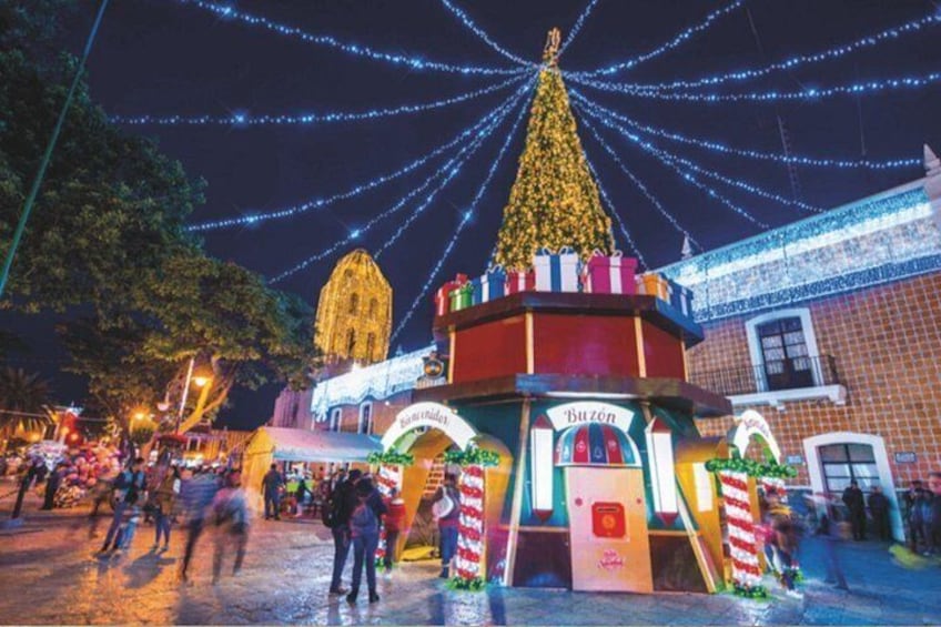 Et festligt marked med et stort juletræ, oplyste bygninger og en traditionel bod. 1