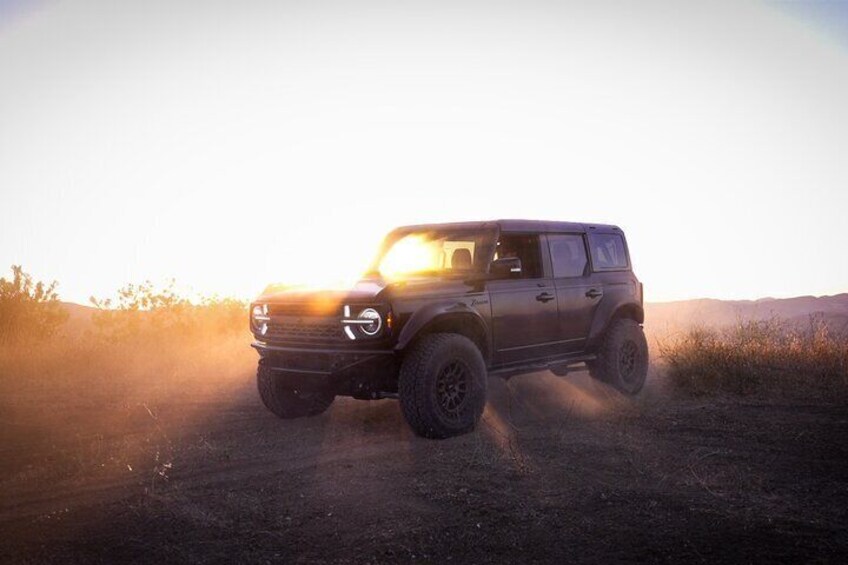A dark-colored SUV driving on a dirt road with a sunset in the background. 5
