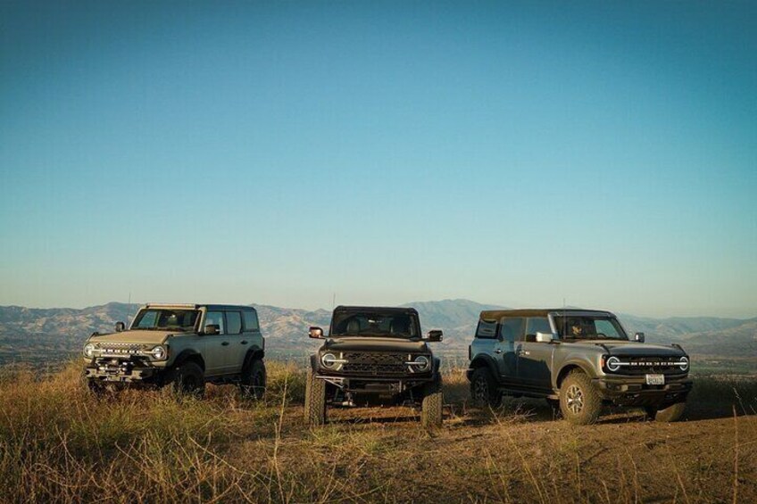 Three off-road vehicles parked on a grassy hill with a mountainous landscape in the background. 4