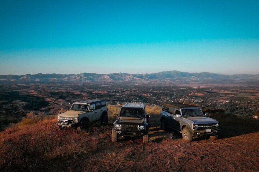 Three off-road vehicles parked on a hill overlooking a valley. 1