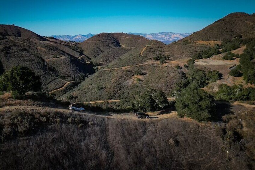A hilly landscape with a dirt road, a white car, and a small building. 3