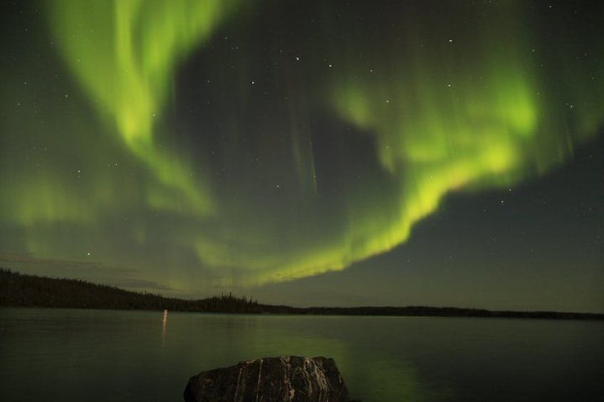 Nordlys over en rolig sø med en sten i forgrunden. 1