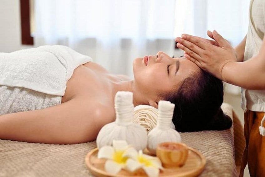 A person receiving a massage with a towel, a bowl of flowers, and a bottle of oil on a massage table. 2