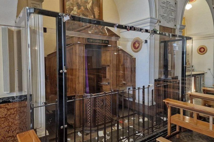 A glass enclosure with a wooden structure inside, a bench outside, and a plaque on the wall. 4