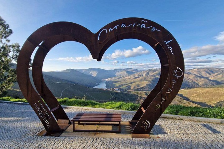 A heart-shaped metal structure with inscriptions, a bench, and a scenic mountain view. 1