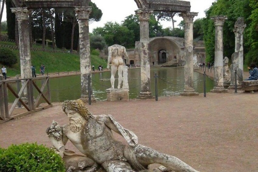 Ancient ruins with statues and columns, a pond, and a pathway. 4