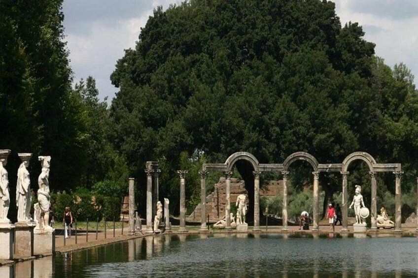 Ancient ruins with statues and columns by a body of water. 3