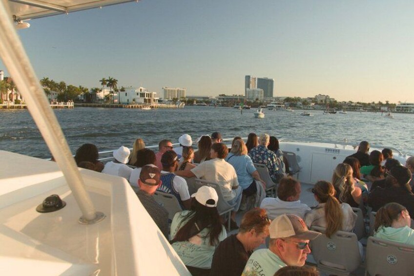 A group of people on a boat, facing a cityscape with buildings and palm trees along the waterfront. 2