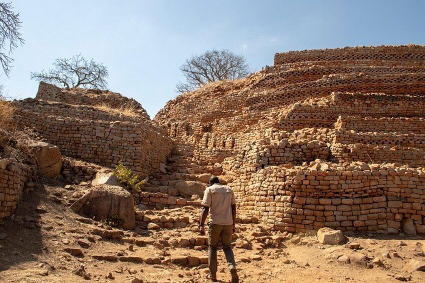 Una persona de pie frente a ruinas de ladrillo antiguo bajo un cielo despejado. 1