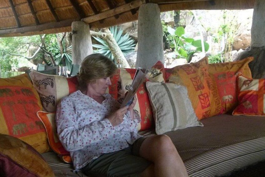 Una persona sentada en un sofá bajo un techo de paja, leyendo un libro. 5