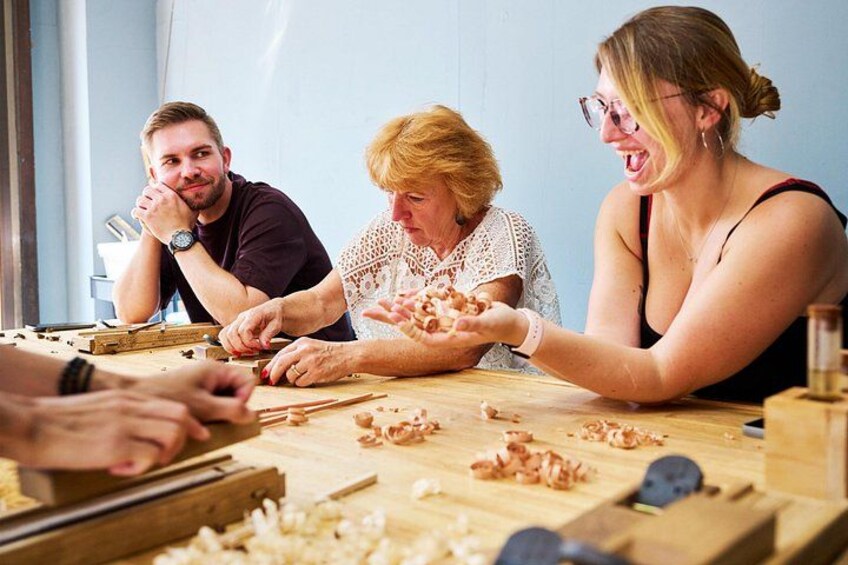 Un groupe de personnes est occupé à travailler le bois, avec des outils et des copeaux de bois sur une table. 3