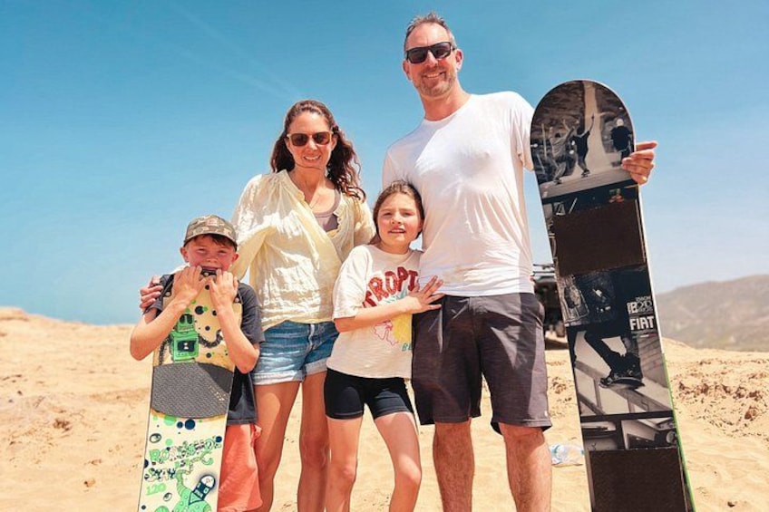 Eine vierköpfige Familie mit einem Snowboard an einem Wüstenstrand. 1