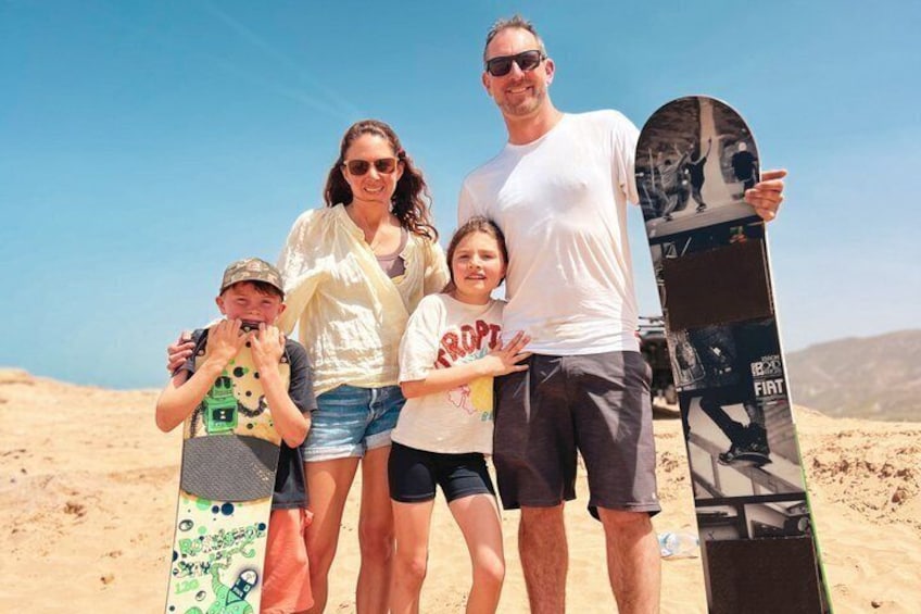 A family on a sandy beach holding a snowboard. 1