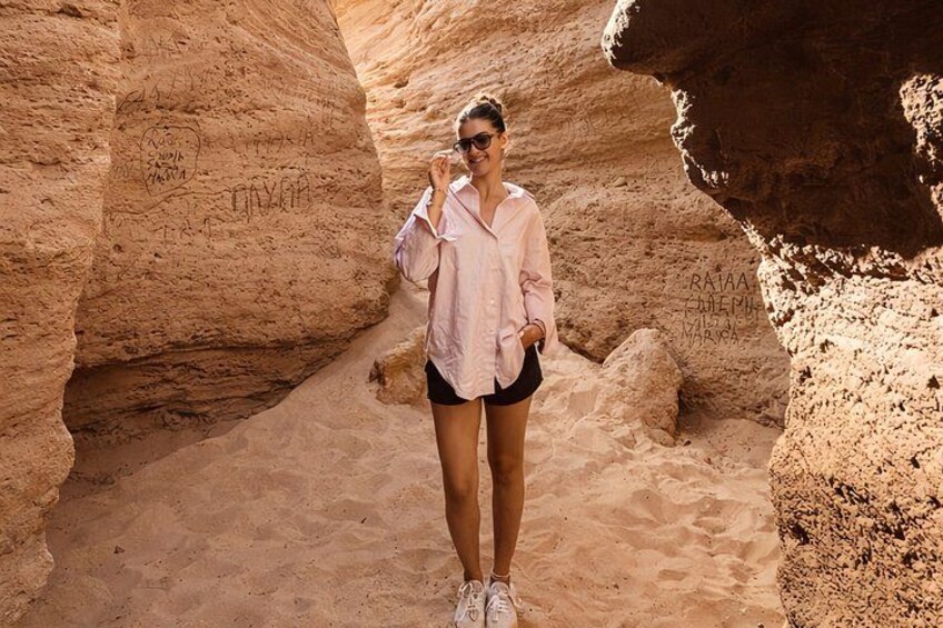A person standing in a narrow canyon with rock walls and a sandy floor. 3