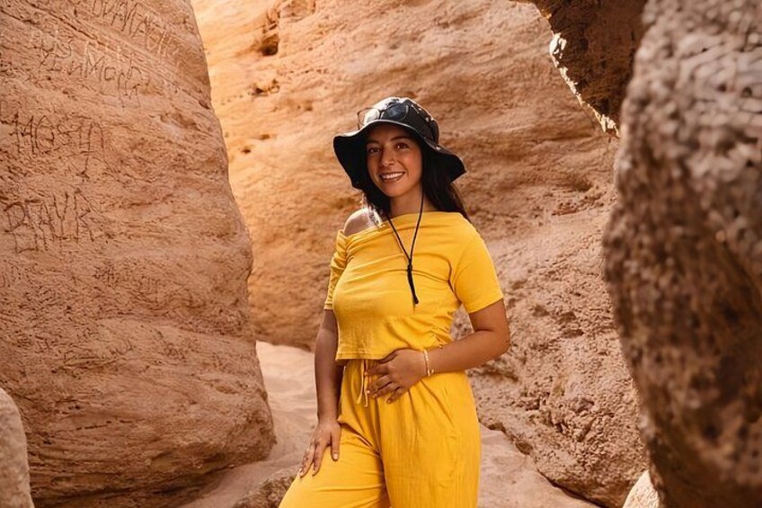 A person in a yellow outfit standing in a rocky canyon with inscriptions on the rocks. 5