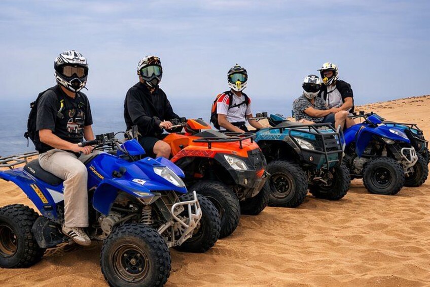 Four people on ATVs on a sandy beach with the ocean in the background. 1