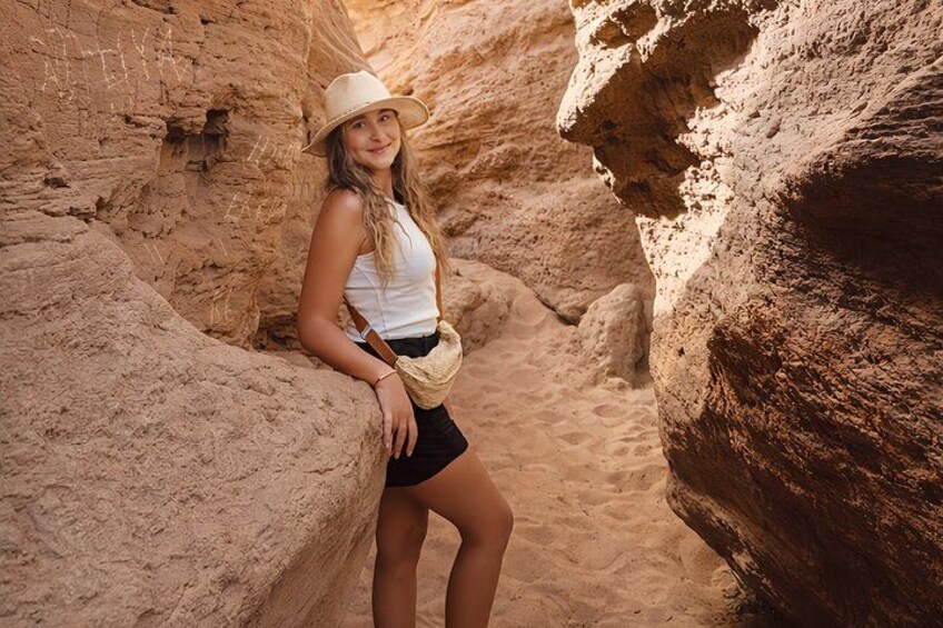 A person leaning against a rock in a narrow canyon with a sandy floor. 2