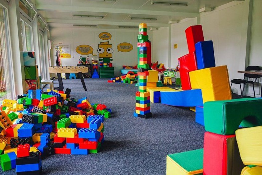 A room filled with colorful building blocks, a tall tower, and a table with a chair. 3