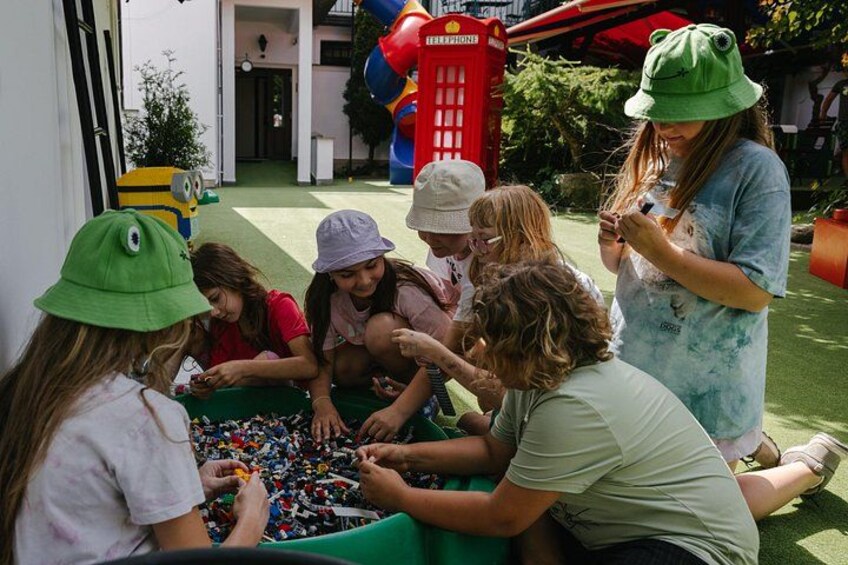 Children playing with colorful beads, a red telephone booth, and a Minion character in a garden. 4