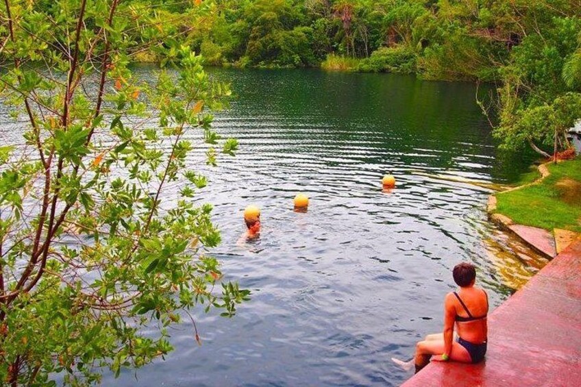 Une femme en bikini est assise sur une structure rouge, près d’un lac paisible bordé d’arbres et de bouées jaunes. 4