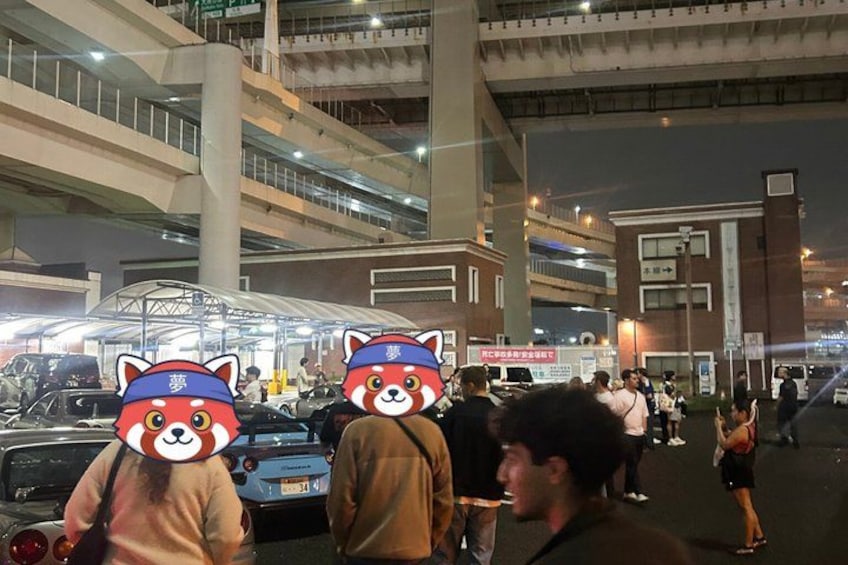 A busy urban street at night with multiple levels of overpasses, a covered market area, and people walking. 3