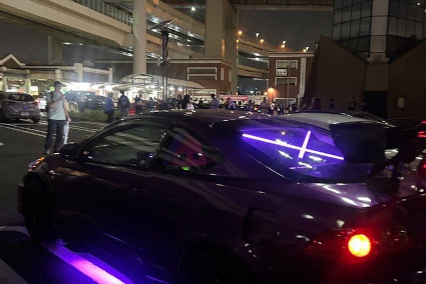 A purple car with neon lights on the roof parked on a street. 2