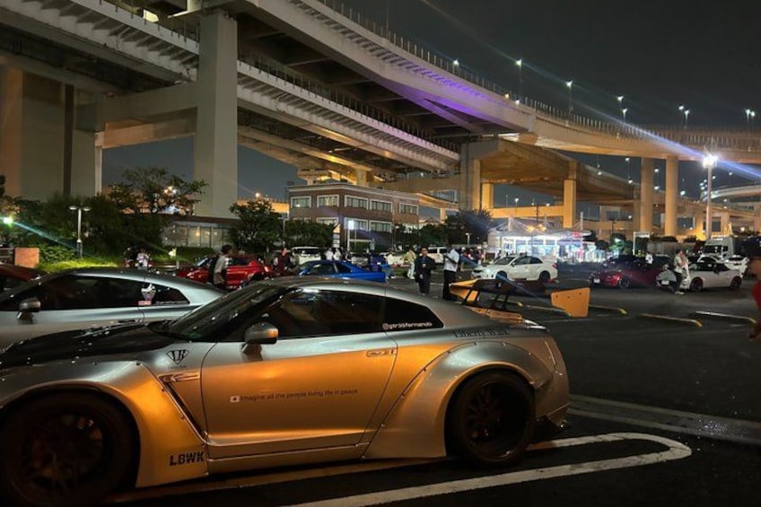 A sports car parked in a busy urban area with a bridge and buildings in the background. 5