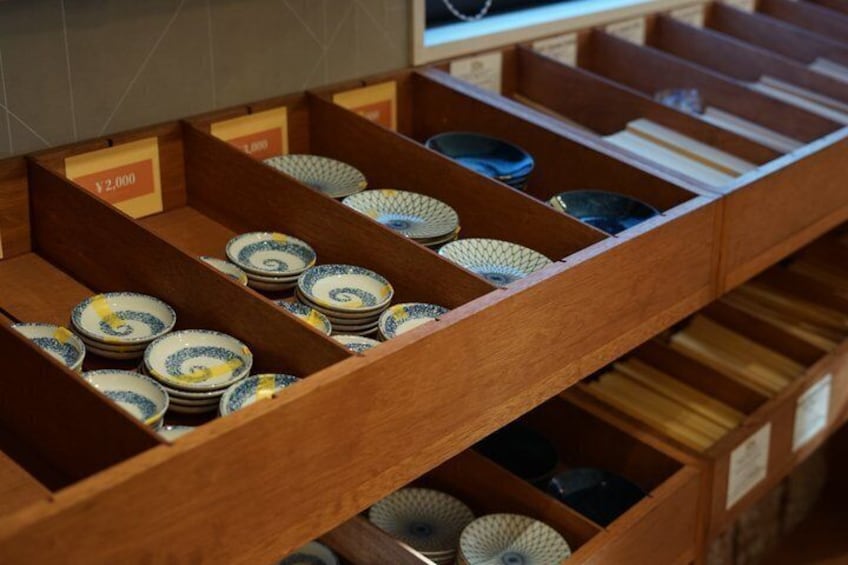 A wooden display case with ceramic plates and bowls, some labeled with prices. 2