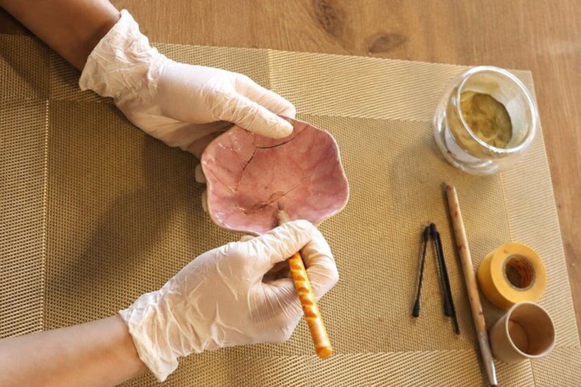 Eine Person mit Handschuhen hält ein pinkes Objekt, vermutlich ein Herz, auf einer gewebten Matte. 5