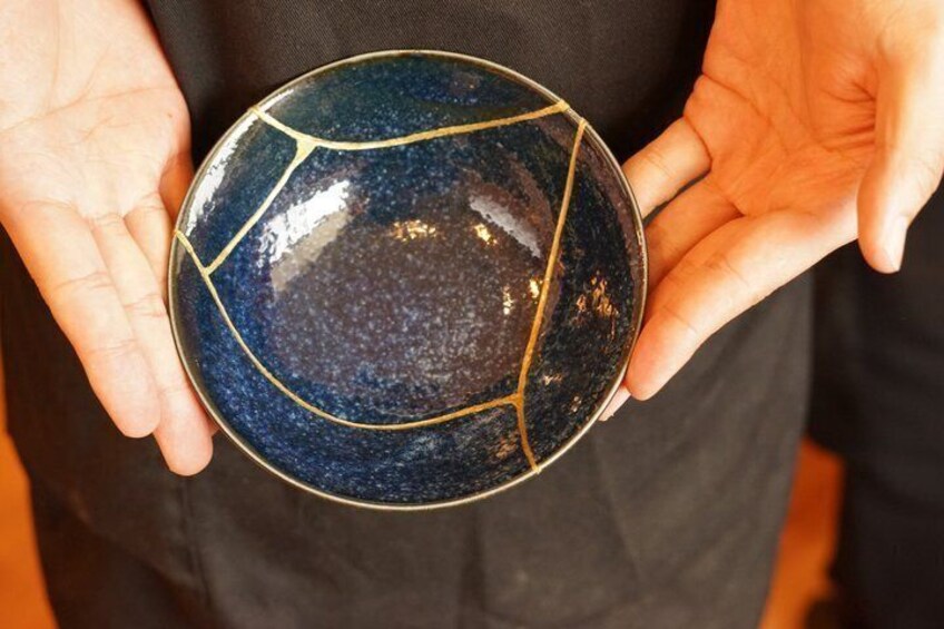 Eine Person hält eine dunkelblaue Keramikschale mit goldfarbenen Linien. 5