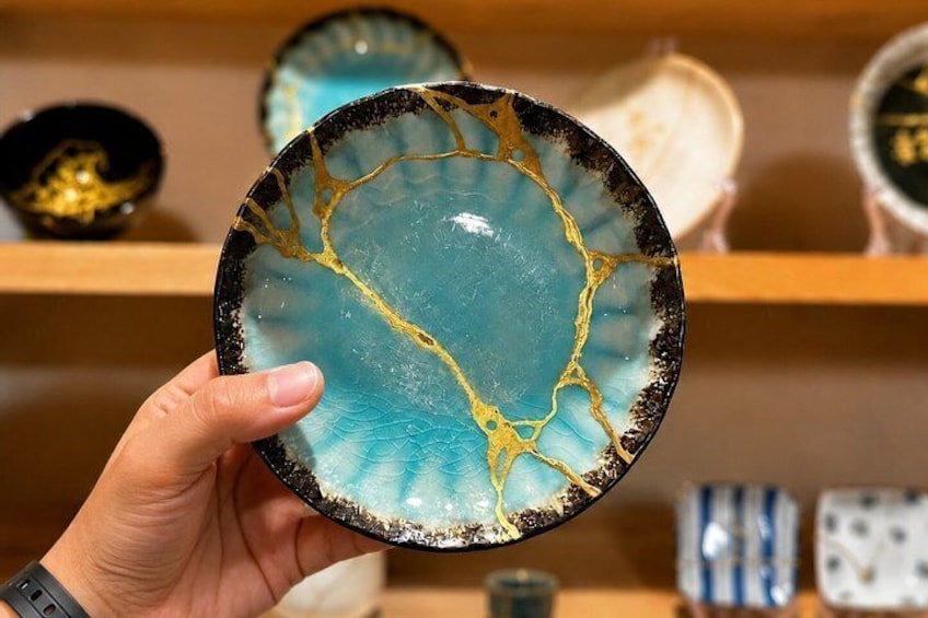 Eine Hand hält einen Keramikteller mit blauem und goldenem Dekor. 1