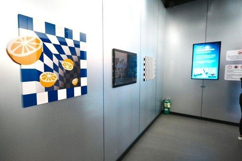 En gang med billedkunst med skakmønster, et indrammet billede, en digital skærm og en brandslukker. 2