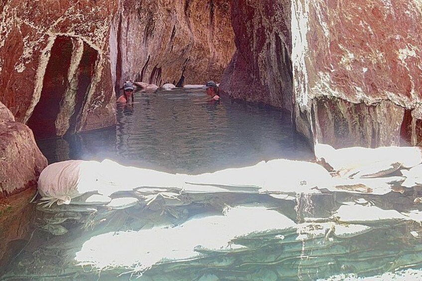 A cave with clear water, people swimming, and large rocks. 2