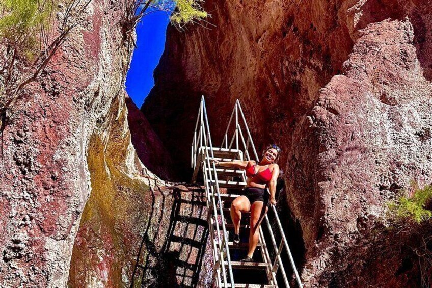 A person climbing a metal ladder in a rocky canyon with a blue sky above. 4