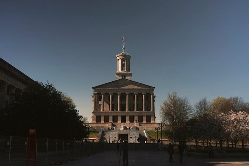 A large neoclassical building with a central dome and columns, surrounded by a plaza with trees and a few people. 3