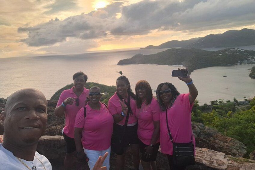 Een groep mensen in roze shirts die poseren bij een kustlandschap met een zonsondergang. 3