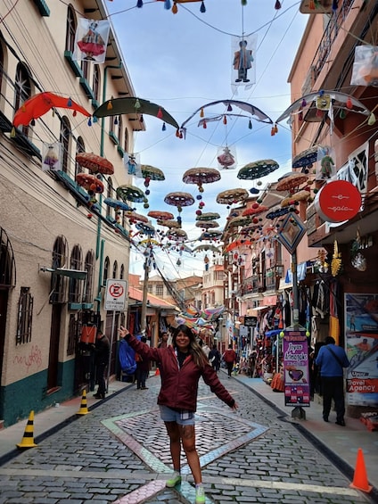 A narrow street with cobblestone pavement, colorful umbrellas hanging overhead, and various shops and signs. 4