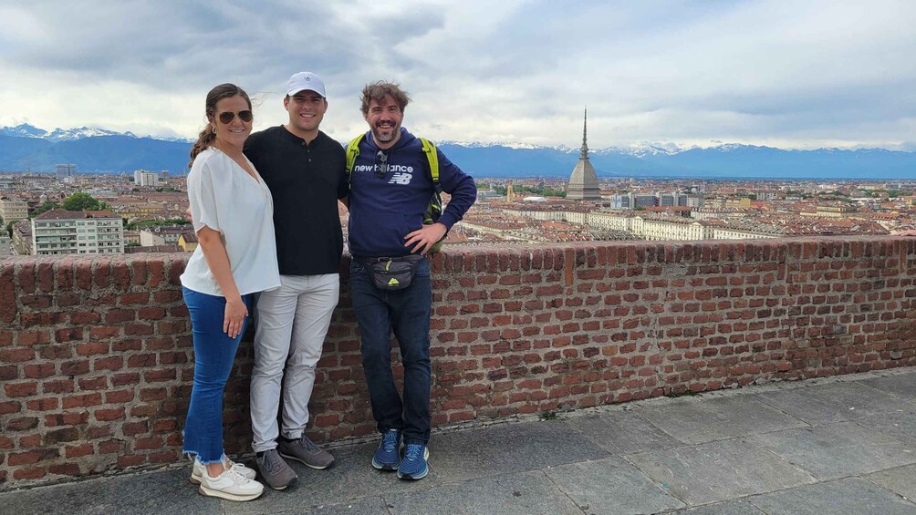 Three people standing on a brick wall with a cityscape and mountains in the background. 5