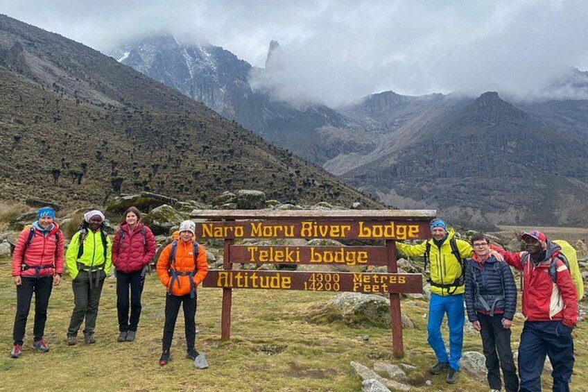 A group of hikers at a mountain lodge sign with altitude information. 5
