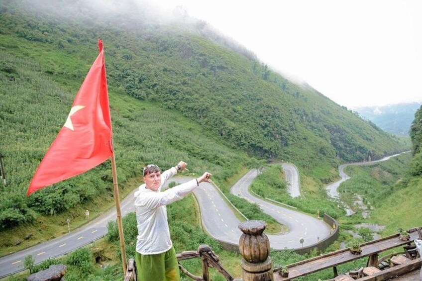 A winding road, a red flag, and lush green hills. 2