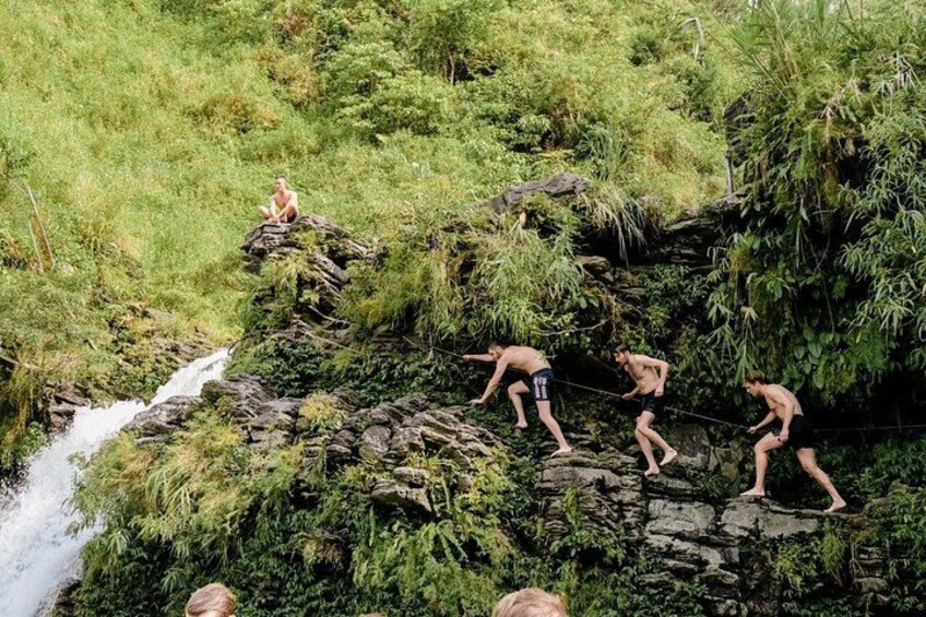 A group of people climbing a rocky, vegetated slope with a stream at the base. 3