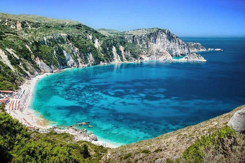 A coastal landscape with a clear blue sea, a sandy beach, and steep cliffs. 4