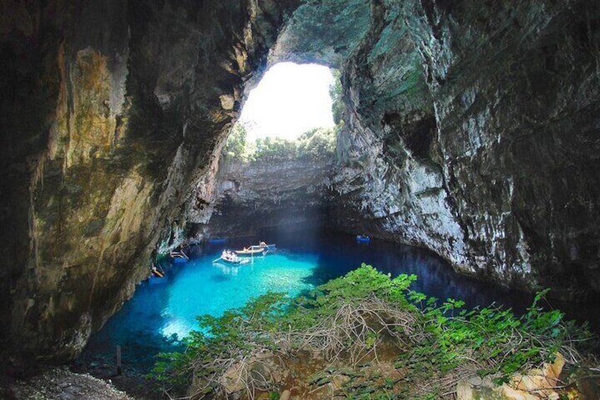 A cave with a clear blue pool, a boat, and lush greenery. 2